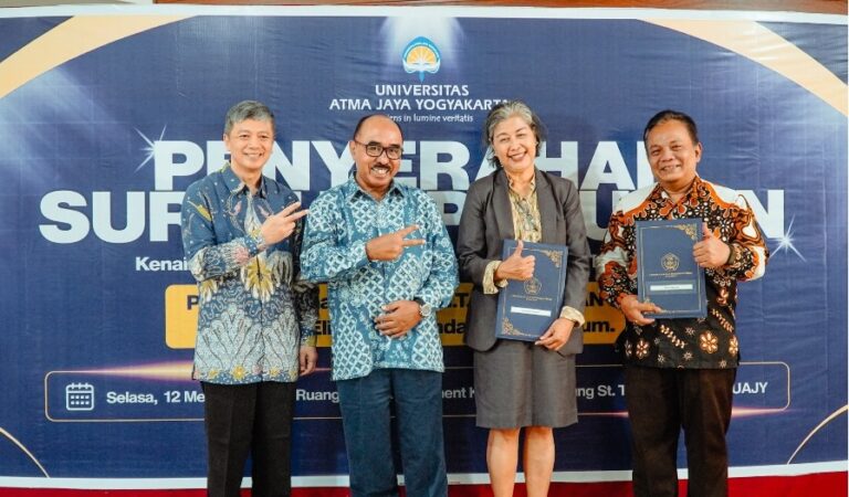 Four people stand in a row, each holding a dark blue certificate folder, smiling for a photo at a university ceremony against a blue banner backdrop.
